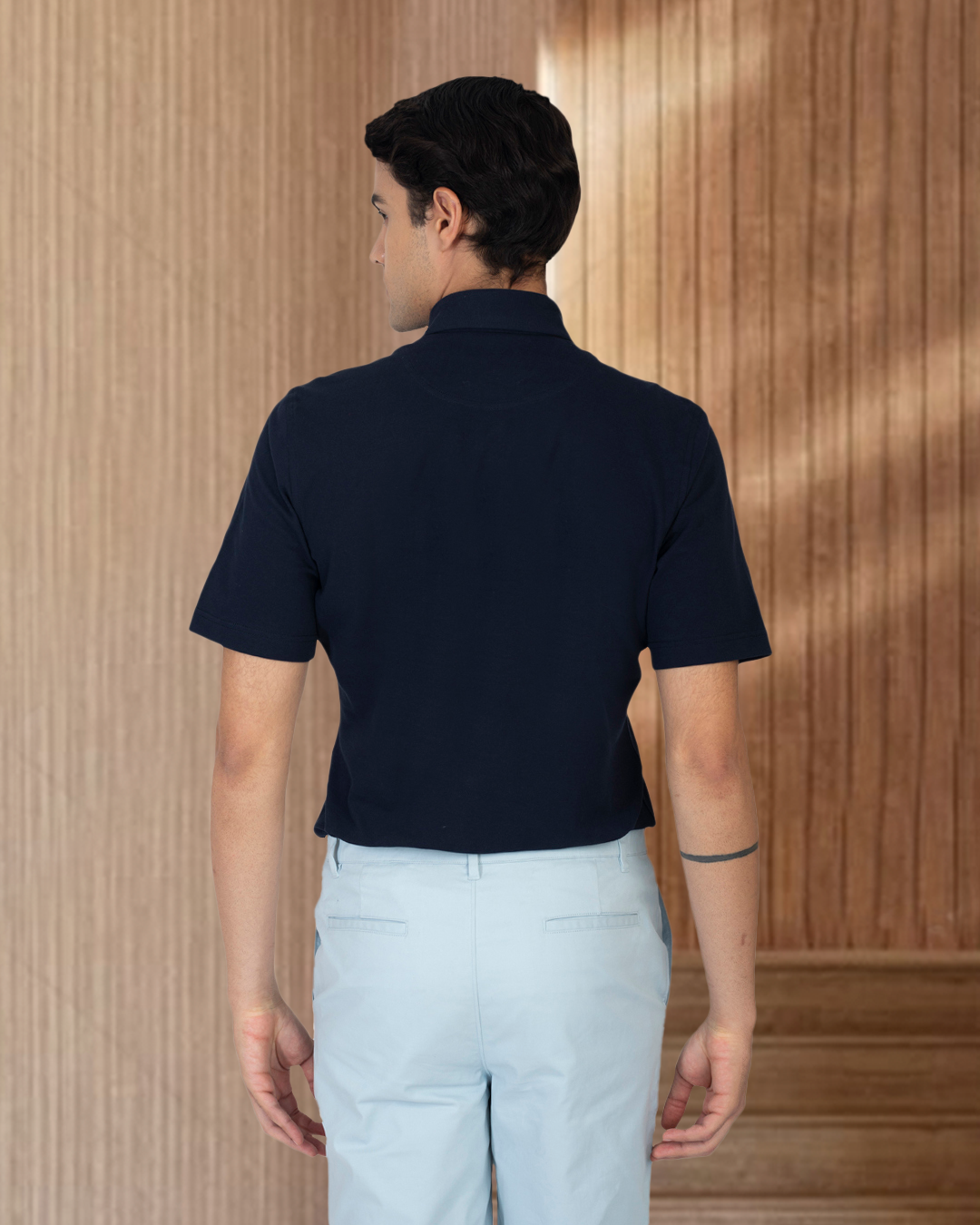 Back of model wearing the custom oxford polo shirt for men by Luxire in navy with white pants 2