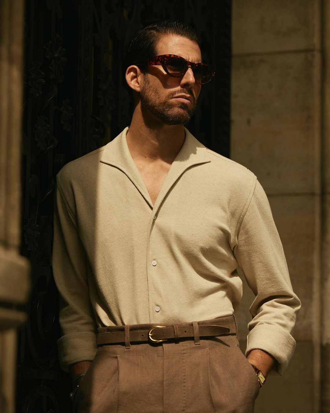 Model wearing custom linen canvas pleated pants for men by Luxire in brown wearing sunglasses