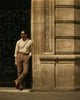 Model leaning wearing custom linen canvas pleated pants for men by Luxire in brown