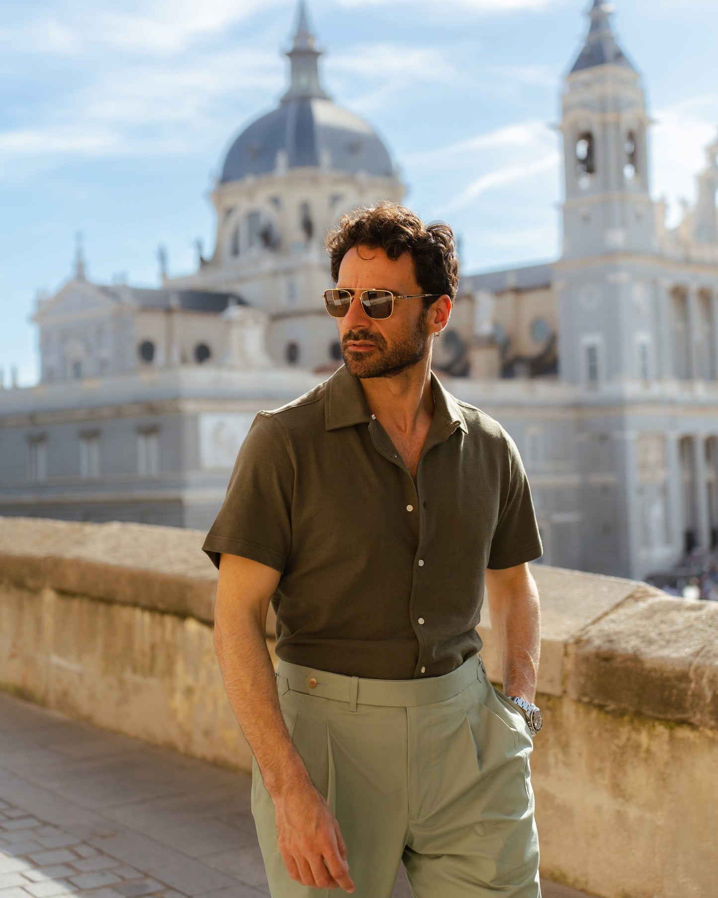 Model outside wearing mens custom polo cotton camp shirt by Luxire in olive green hand in pocket 5